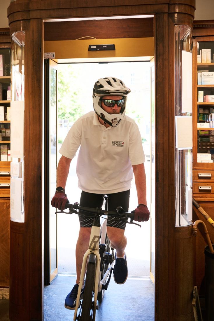 Ein Radfahrer mit Helm fährt durch die Eingangstür der Apotheke