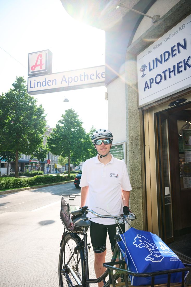 Ein Radfahrer mit blauer Transportbox steht vor dem Eingang der Linden-Apotheke